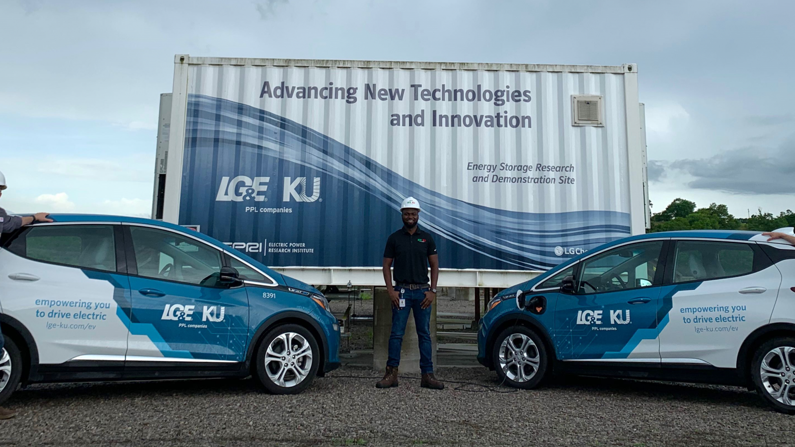 three employees standing next to electric vehicles and large battery storage unit