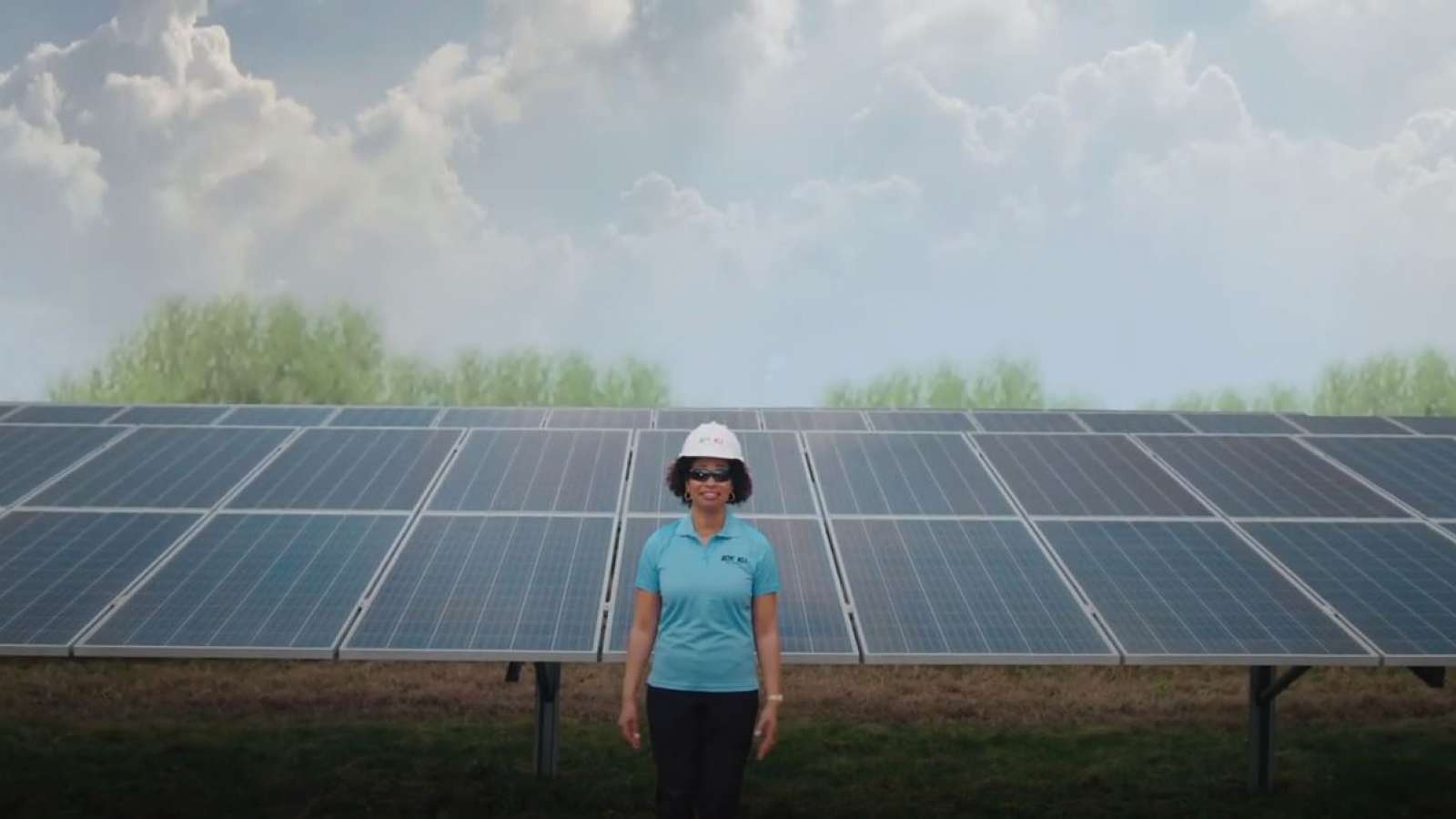 employee wearing hard hat standing in front of a solar array